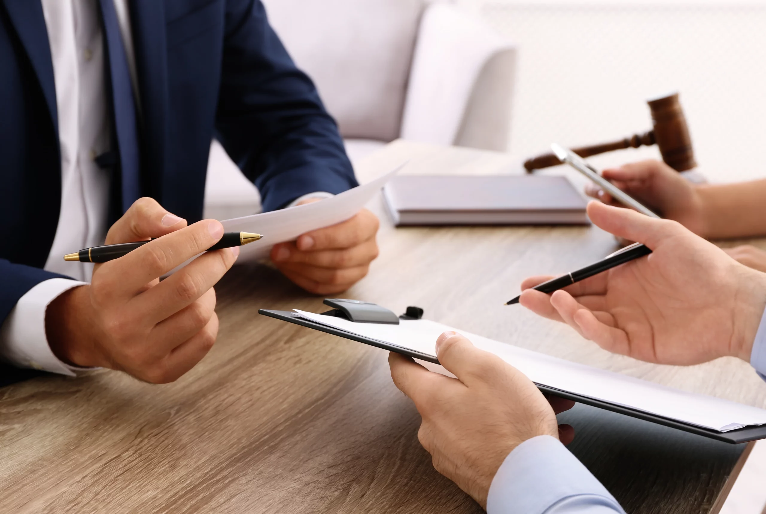 Close‑up of people at a table with pens, paper, clipboard, gavel, and notebook, illustrating a Chapter 7 341 meeting of creditors in Milwaukee.